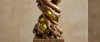 Wooden carved sculpture featuring intertwined ribbons and grape clusters on pedestal base, showcasing traditional craftsmanship and organic flowing design elements.
