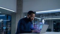 African American businessman working late on laptop with holographic data display in modern office environment for technology and innovation concepts.