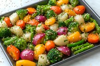 Colorful roasted vegetables with broccoli, potatoes, cherry tomatoes and red onions seasoned with herbs and spices on baking sheet, ready for healthy meal prep.