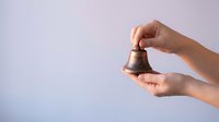 Hands holding a vintage bronze bell against a soft light background, evoking nostalgia, alerts, and classic school or service concepts.