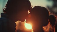 Romantic couple silhouettes kissing at sunset with warm golden light creating intimate moment between two people in love during golden hour outdoors.