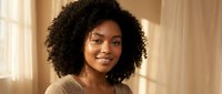 Young African American woman with curly hair smiling warmly in soft natural light wearing beige sweater for lifestyle and portrait photography.