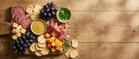 Gourmet charcuterie board with assorted meats, cheeses, grapes and crackers on rustic wooden background for entertaining and appetizer presentations.