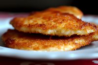Crispy golden chicken cutlets with breaded coating stacked on white plate, close-up macro shot showing delicate texture and savory crust details.