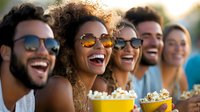Diverse group of young friends enjoying outdoor movie night with popcorn, sharing genuine laughter and joy while wearing sunglasses on summer evening.