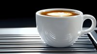 White ceramic cup filled with fresh cappuccino showing latte art heart pattern on dark background with dramatic side lighting and metal surface.