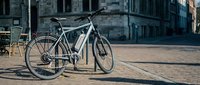 White electric hybrid bicycle parked on urban brick street with historic buildings, sustainable city commute and eco-friendly transportation solution.