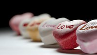 Candy hearts with love text messages arranged in line on white surface with selective focus and soft bokeh background. Romance and Valentine's Day concept.