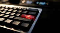 Close-up of computer keyboard with glowing red enter key in dark environment, dramatic lighting for cybersecurity and technology concepts.