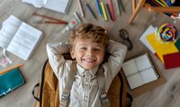 Happy elementary school student lying on floor surrounded by books, notebooks and school supplies, relaxing with hands behind head during homework break.