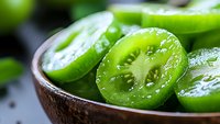 Fresh sliced green tomatoes in wooden bowl, macro view showing juicy texture and seeds. Natural organic produce with vibrant color and water droplets.