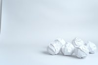 Crumpled white paper balls scattered on white surface creating minimalist composition with soft shadows. Clean modern design background for business concepts.