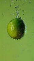 Fresh lime floating in water with splashing droplets against green background, creating dynamic motion and refreshing atmosphere for beverage advertising.