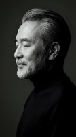 Mature Asian man with gray beard in black turtleneck smiling peacefully in profile portrait. Monochrome studio photography for professional headshots.