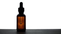 Amber glass dropper bottle with black rubber bulb and pipette on dark surface against white background for cosmetic and pharmaceutical packaging.