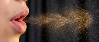 Woman exhaling golden glittery particles from mouth against dark background, magical breath effect for fantasy and wellness concepts.