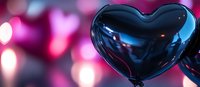 Shiny black heart balloon against blurred pink bokeh background creates romantic atmosphere. Celebration and love concept for Valentine's Day and special occasions.
