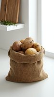 Fresh organic potatoes in rustic burlap sack on white kitchen counter with natural lighting for healthy cooking and farm-to-table meal preparation.