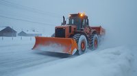 Orange snow plow truck clearing snowy road during winter storm with low visibility conditions, working in residential area with power lines visible in background.