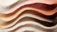 Flowing waves of natural earth tone makeup powder creating smooth gradient layers in warm brown beige coral shades for cosmetic beauty applications.