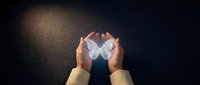 Hands cupping glowing geometric crystal formation with ethereal light effects against dark textured background for spiritual and energy healing concepts.