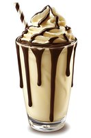 Vanilla milkshake with chocolate syrup drizzle and whipped cream topping in tall glass with striped straw isolated on white background for dessert menu design.