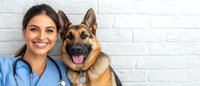Young female veterinarian in blue scrubs with stethoscope smiling next to happy German Shepherd dog against white brick wall background, healthcare concept.