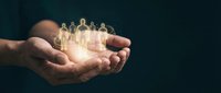Hands holding glowing human figures representing teamwork, leadership and community support in business concept with warm light effect.