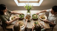 Family of four sharing healthy meal together at wooden table with fresh salads and vegetables, overhead view for dining and nutrition content.