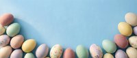 Colorful pastel Easter eggs arranged as a border on a light blue background with copy space for text or design.