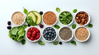 Fresh organic superfoods in white bowls on light background including berries, nuts, seeds, avocado and greens arranged in modern flat lay composition.