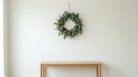 Evergreen wreath with natural foliage hanging on neutral wall above wooden console table, suitable for holiday home decor and seasonal interior design projects.