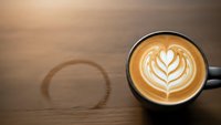 Coffee cup with heart latte art on wooden table creating circular shadow, perfect for cafe menu design and morning beverage concepts.