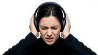 Young woman wearing headphones with frustrated expression showing audio discomfort or loud noise reaction isolated on white background for design use.