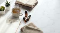 Spa wellness setup with herbal tea, essential oils, soft towels and succulents for relaxation and self-care routine on white marble surface.
