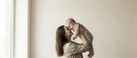 Young Caucasian mother lifting her baby up, sharing a tender nose kiss moment in a bright minimalist room, capturing pure love and joy.