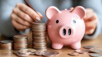 Pink ceramic piggy bank next to ascending stacks of coins on wooden table with hands arranging money, representing savings growth and financial planning.
