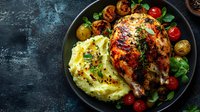 Roasted chicken breast with creamy mashed potatoes, colorful cherry tomatoes and fresh herbs in cast iron skillet for gourmet dinner presentation.