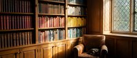 Cozy library interior with wooden bookshelves filled with colorful books, leather armchair and diamond-paned window creating warm reading atmosphere.