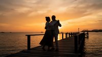 Silhouette of couple embracing on wooden dock at golden sunset over calm water, romantic evening scene for love and relationship concepts.