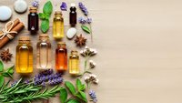 Natural essential oils in amber bottles with fresh herbs, spices and aromatherapy ingredients arranged on wooden background for wellness and spa treatments.