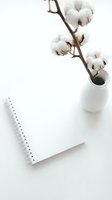 Minimalist flat lay with spiral notebook and cotton branch in white vase on clean desk, soft natural aesthetic for lifestyle blogs.