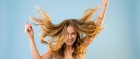 Young blonde woman with flowing hair dancing joyfully against blue sky background, expressing freedom and happiness in carefree moment outdoors.