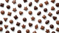 Assorted chocolate candies in various shapes including hearts, stars, spheres and cubes arranged on white background for confectionery and dessert designs.