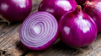 Fresh red onions sliced and whole on rustic wooden background, vibrant purple color and detailed texture showing concentric rings in natural lighting.