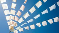 White paper flags or bunting hanging on strings against bright blue sky creating festive outdoor celebration atmosphere for parties and events.