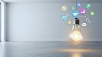 Glowing light bulb with colorful business icons floating above in modern office interior representing innovation, creativity and digital transformation.
