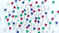 Colorful heart-shaped gemstones and diamonds scattered on white background. Precious stones in red, blue, green colors with sparkling crystals for jewelry design.