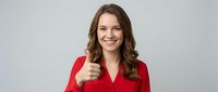 Young professional woman in red blazer giving thumbs up gesture with confident smile against neutral background for business success concepts.