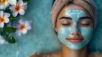 Young Asian woman relaxing with blue clay mask facial treatment at spa, plumeria flowers on turquoise background, eyes closed, wrapped in towel.